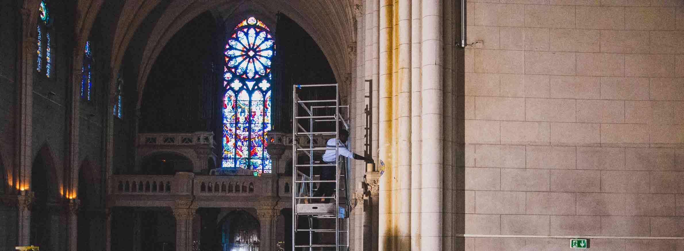 Chantier de rénovation d'une chapelle, un ouvrier change une lampe en hauteur.